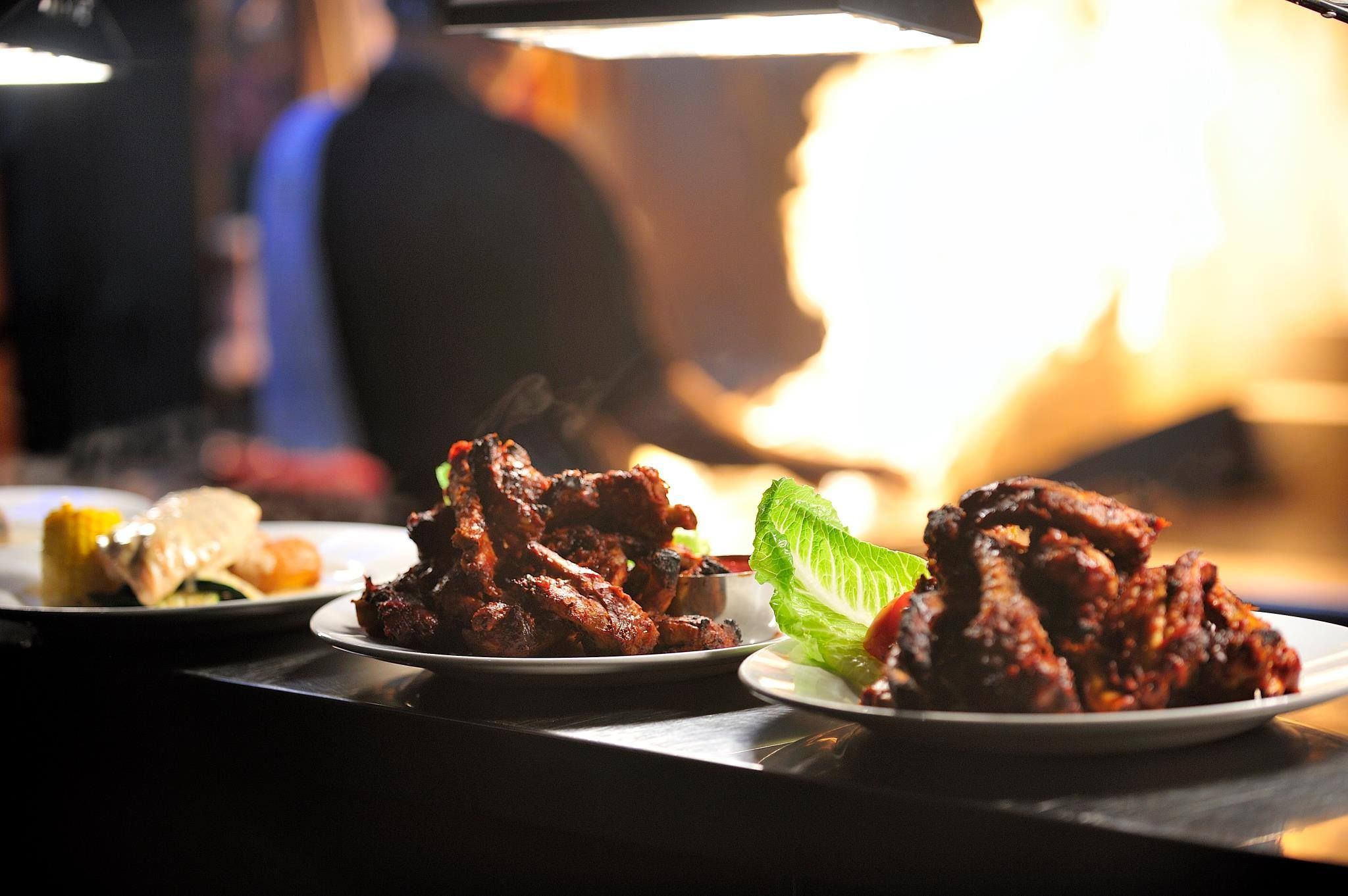 Ribs and wings on the pass, the grill flaring behind